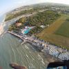 Vista aerea di una costa con spiaggia, campi, e strutture turistiche accanto al mare.