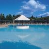 Grande piscina con isola centrale e ombrellone, cielo azzurro e nuvoloso.