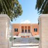 Villa arancione con colonne bianche, circondata da palme e un vialetto di pietra.