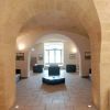 Interno di una sala con ampio arco, pavimento in pietra e arredamento sobrio.