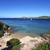 Costa rocciosa con mare blu e una barca a vela.
