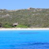 Spiaggia con mare blu e vegetazione collinare.