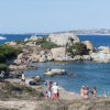 Persone su una spiaggia rocciosa con mare limpido e barca sullo sfondo.