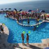 Un'affollata piscina all'aperto con persone che giocano con palloncini colorati, vista mare.