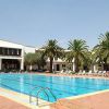 Piscina all'aperto con lettini e palme, edificio sullo sfondo.