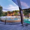 Una piscina circondata da sdraio su una terrazza in legno, con alberi attorno.