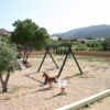 Parco giochi con altalene e scivoli su sabbia.