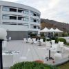 Terrazza di un edificio bianco con tavoli e sedie, colline sullo sfondo.