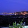Vista notturna di una costa illuminata con colline sullo sfondo e luci lontane.