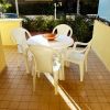 Un tavolo rotondo bianco con cinque sedie bianche su un patio piastrellato.