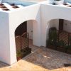 Cortile con archi bianchi, pareti intrecciate e piante in fioriere.