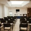Sala conferenze con sedie nere, un podio e uno schermo televisivo.