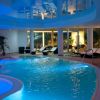 Piscina interna illuminata, circondata da lettini e piante, con struttura moderna a colonne.