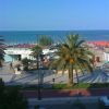 Spiaggia con palme, cabine, ombrelloni arancioni e mare azzurro sullo sfondo.