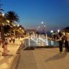 Passeggiata serale con fontane illuminate accanto a palme.