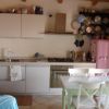 Cucina moderna con mobili chiari, tavolo con sedie e frigorifero rosa.