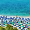 Spiaggia sabbiosa con numerosi ombrelloni blu e mare turchese.