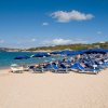 Spiaggia con sabbia chiara, ombrelloni blu e lettini, mare calmo e cielo azzurro.
