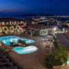 Vista notturna di un hotel con due piscine illuminate e città in lontananza.