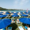 Lettini e ombrelloni blu su erba, vicino a una spiaggia sabbiosa.