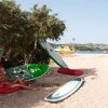 Una donna seduta su un cuscino rosso sotto un albero vicino a tavole da surf sulla sabbia.