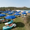 Lettini bianchi con ombrelloni blu su un prato verde vicino a una spiaggia.