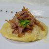 Piatto di raviolo con pancetta croccante e foglia verde sopra.
