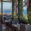 Veranda di un ristorante con sedie e tavoli, vista mare e vegetazione rampicante.