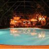Piscina illuminata di notte, con sedie a sdraio attorno e un bar sullo sfondo.