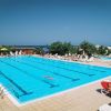 Ampia piscina con corsie, persone che nuotano e rilassano sulle sdraio sotto un cielo blu.