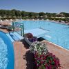 Piscina all'aperto con una passerella galleggiante, circondata da fiori colorati e sdraio.