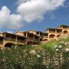 Edifici con archi e balconi su una collina con piante fiorite in primo piano.