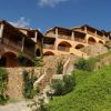 Complesso residenziale con archi e pietra, situato su una collina verde.