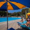 Persone rilassate su sdraio accanto a una piscina con ombrelloni colorati.