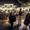 Musicisti che suonano davanti a un pubblico seduto all'aperto di sera.