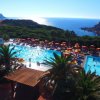 Vista di una piscina con ombrelloni rossi e gialli e il mare sullo sfondo.