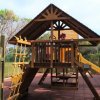 Parco giochi in legno con scivolo giallo e area arrampicata, circondato da recinzione.