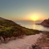 Sentiero costiero al tramonto con vista sul mare e promontorio.