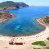 Spiaggia a forma di mezzaluna con mare azzurro e torre su un promontorio.