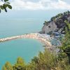 Spiaggia affollata con mare turchese e colline verdi.