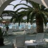 Piscina con sdraio e palme, vista da un arco bianco.