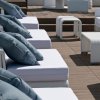 Sedie bianche su un terrazzo di legno, con cuscini grigi e tavolini bianchi.