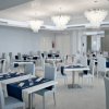 Sala ristorante ampia con sedie grigie, tavoli bianchi e lampadari moderni.