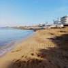 Spiaggia sabbiosa con mare calmo e edifici bianchi sullo sfondo sotto un cielo azzurro.