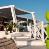 Terrazza di un bar sulla spiaggia con arredi bianchi e un grande vaso verde a forma di tulipano.