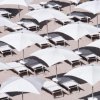 Spiaggia con file di lettini e ombrelloni bianchi disposti geometricamente.