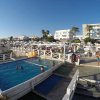 Una piscina con persone che nuotano, ombrelloni bianchi e un edificio sullo sfondo.