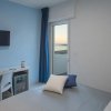 Camera moderna con pareti blu, balcone con vista mare, scrivania, TV e letto con cuscini.