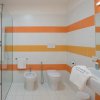 Bagno moderno con doccia in vetro, bidet e wc. Piastrelle bianche con strisce arancioni e gialle.