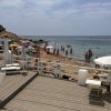 Spiaggia affollata con ombrelloni colorati e persone in acqua; terrazza in legno in primo piano.
